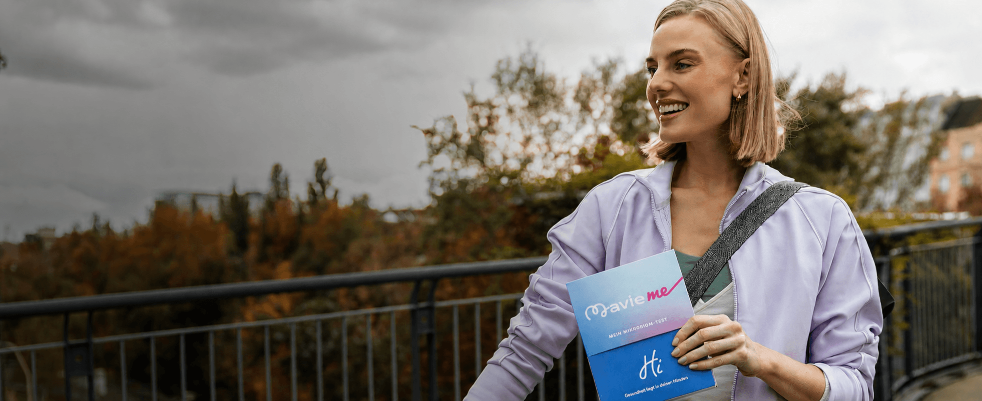 Woman standing beside a bicycle outdoors while holding a MavieMe microbiome test kit, promoting preventive health and an active lifestyle.