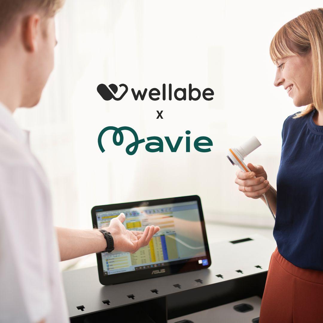 Mavie x wellabe Zwei Personen betrachten gemeinsam Gesundheitsdaten auf einem Bildschirm. Darüber sind die Logos von wellabe und Mavie mit einem „x“ als Kooperationssymbol abgebildet.
