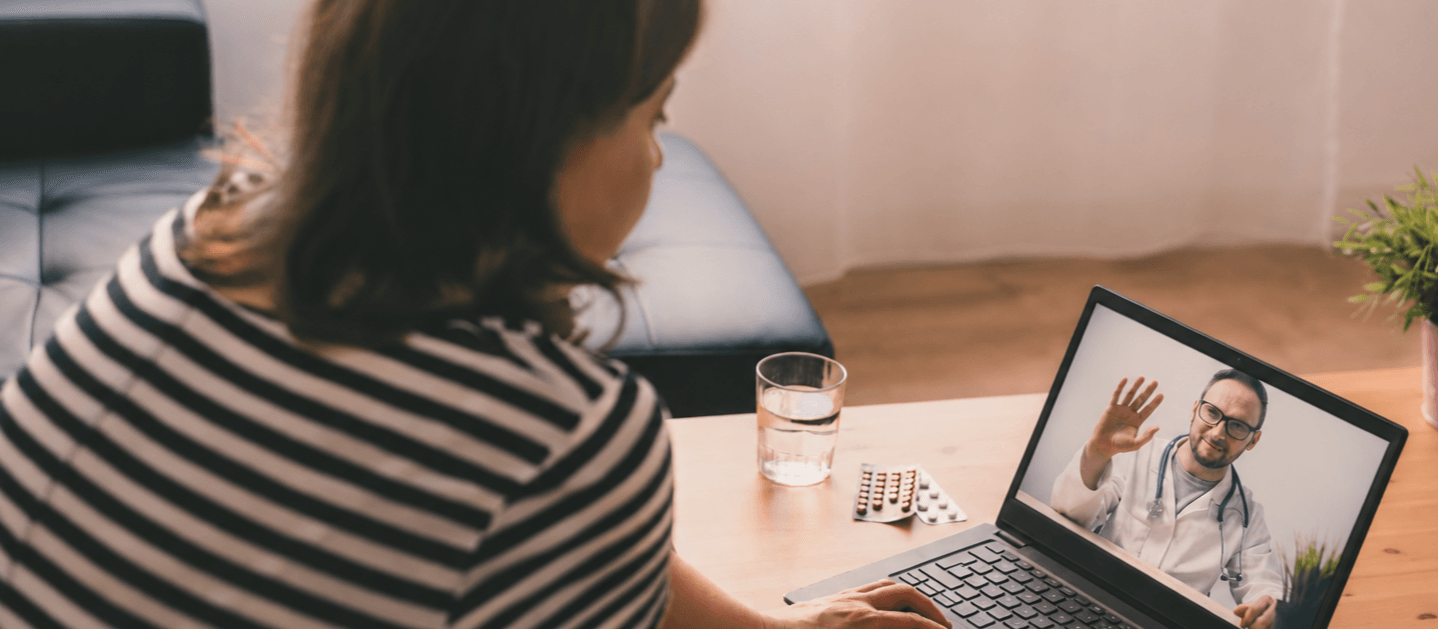 Person attending a video consultation with a doctor on a laptop from home, with medication and a glass of water on the table.