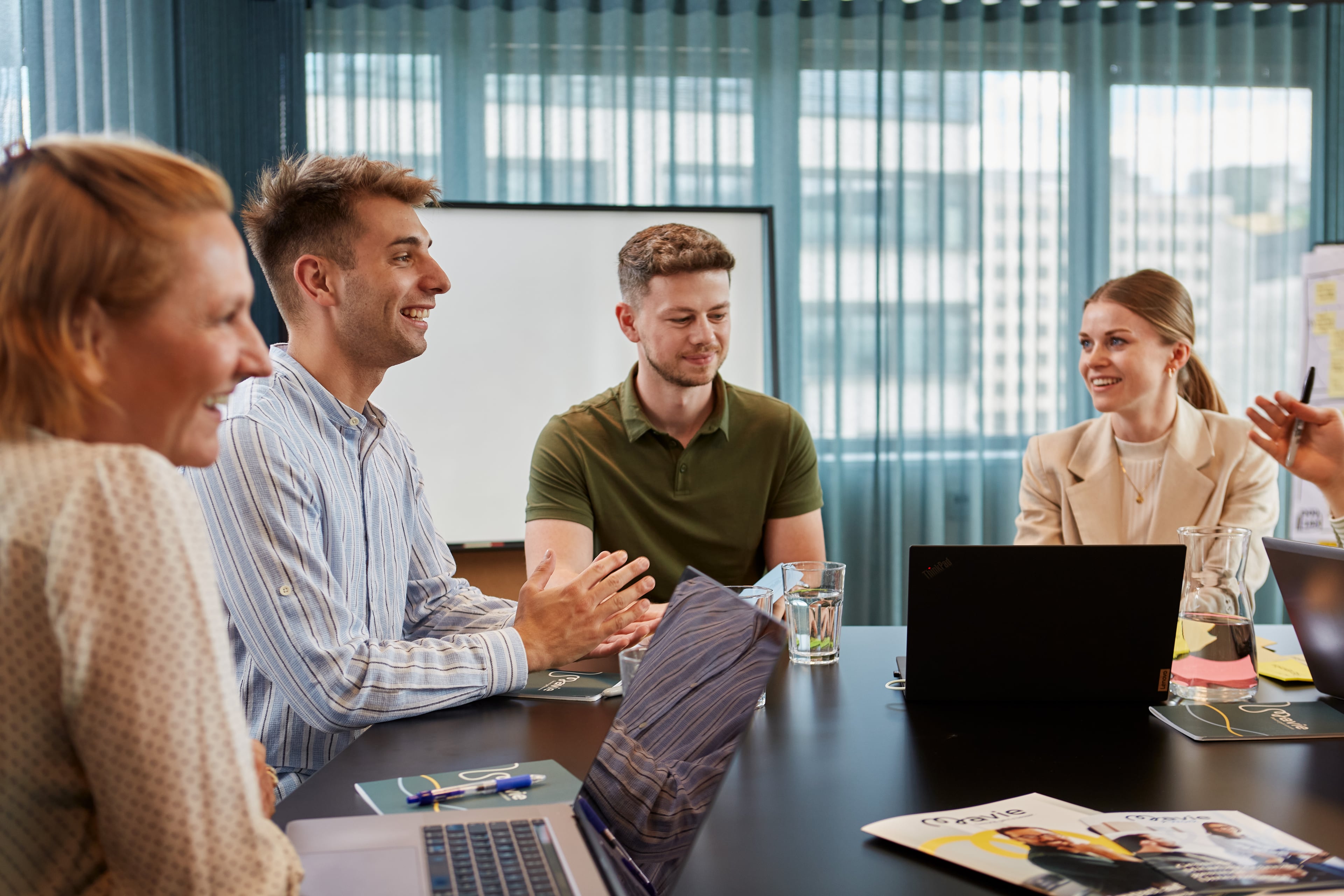 Team von Mitarbeitenden sitzt in einem Besprechungsraum zusammen und diskutiert in einer offenen und positiven Arbeitsatmosphäre.