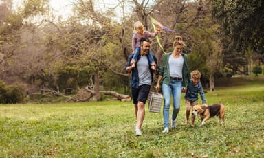 Familie mit zwei Kindern und Hund beim Spaziergang im Park – Symbolbild für Gesundheit, Prävention und ein aktives Familienleben