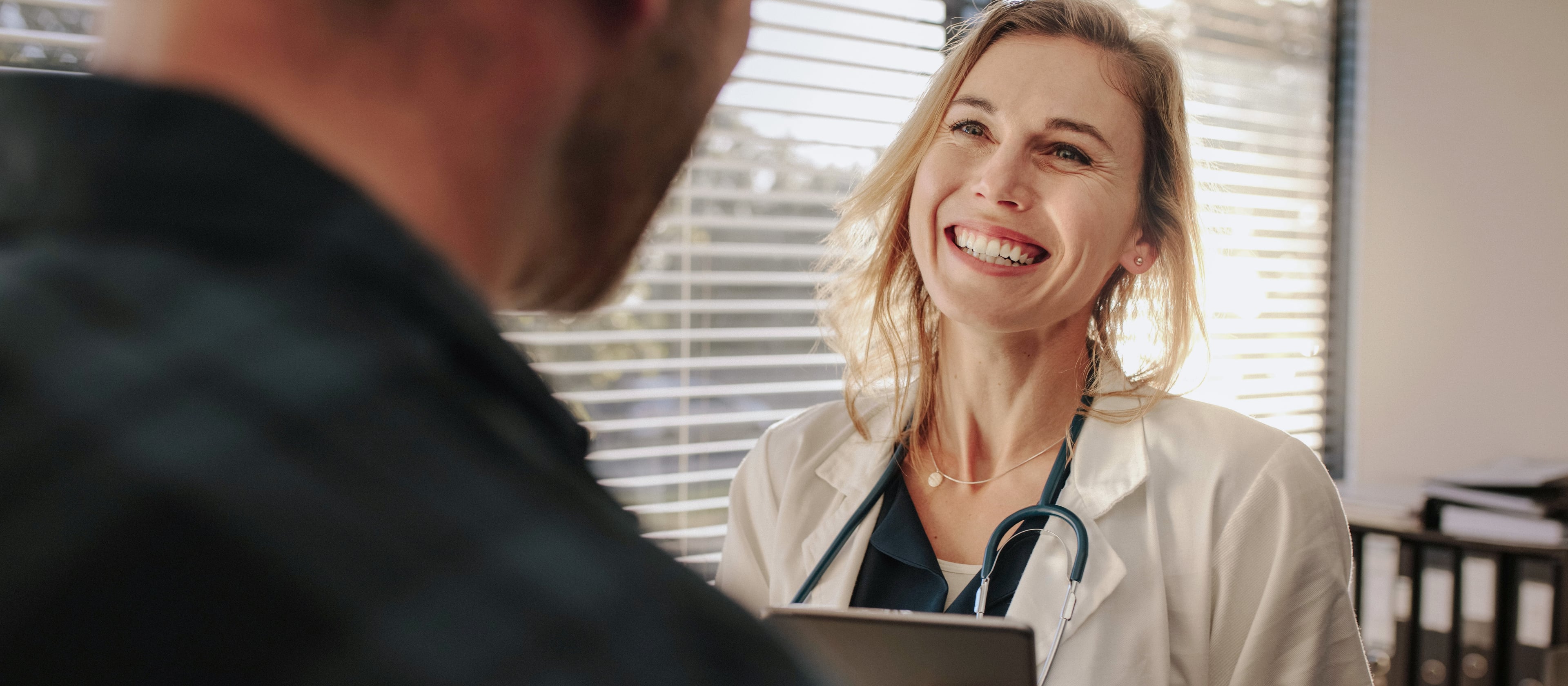 Doctor with a stethoscope speaking warmly with a patient while holding a tablet.