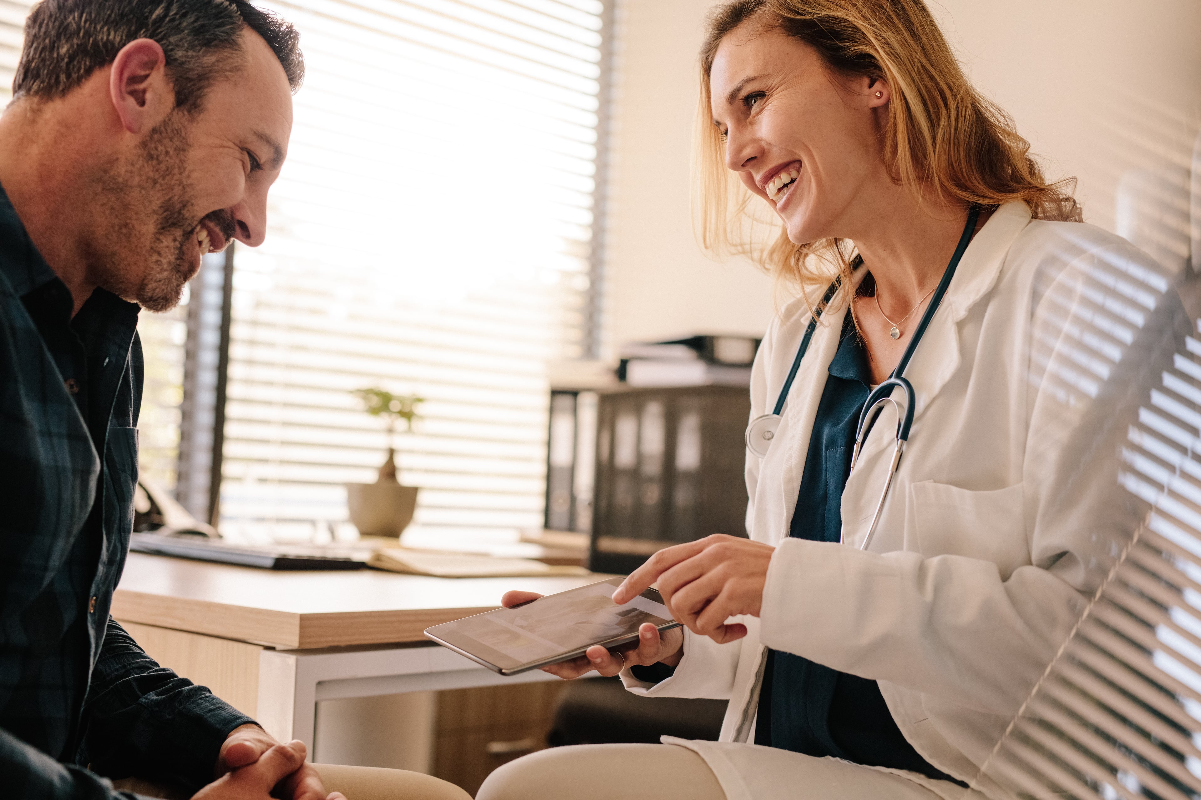 Ärztin bespricht mit einem Patienten auf einem Tablet medizinische Informationen in einer Praxis.