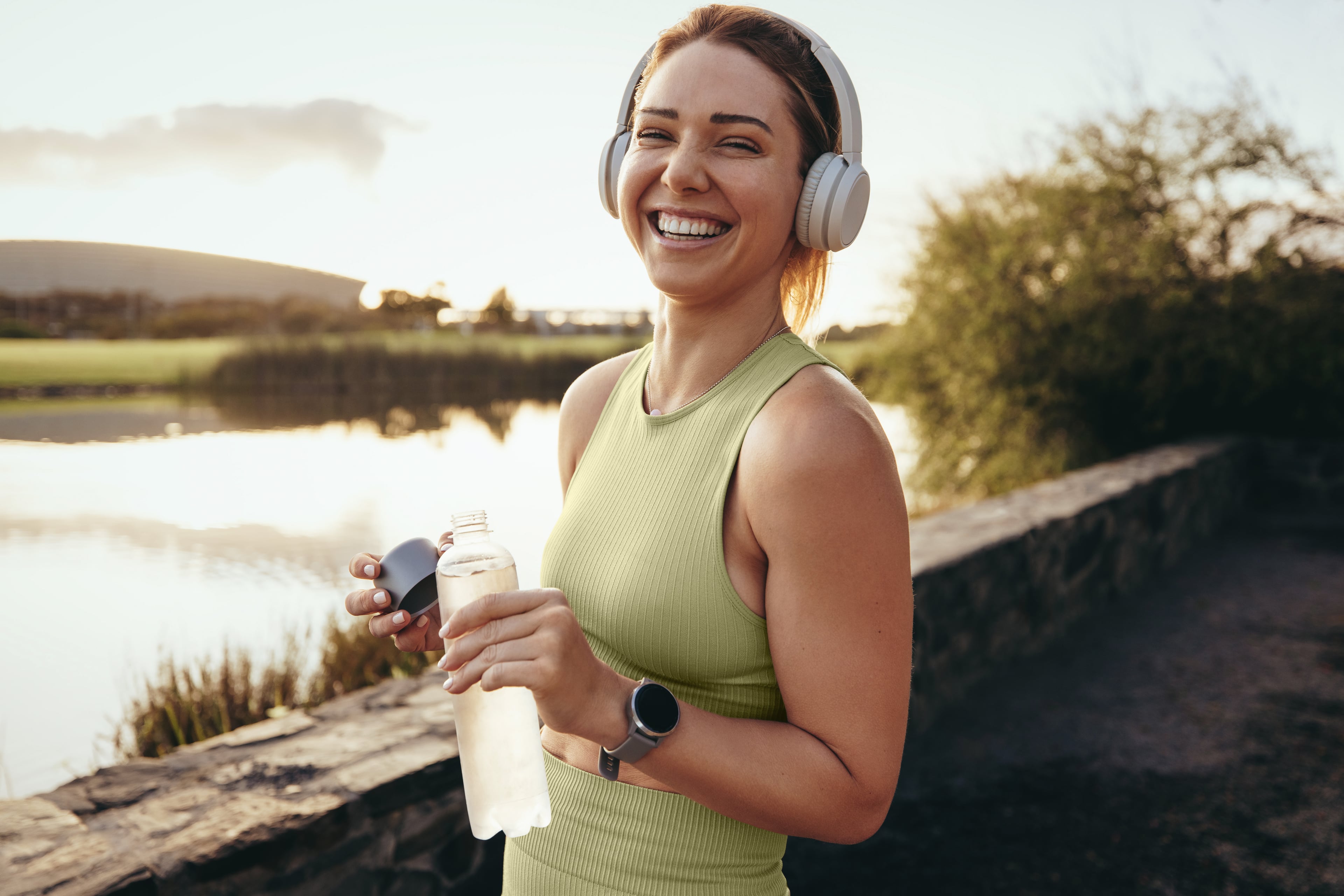 A person stands in a natural landscape wearing athletic clothing. They are holding a water bottle.