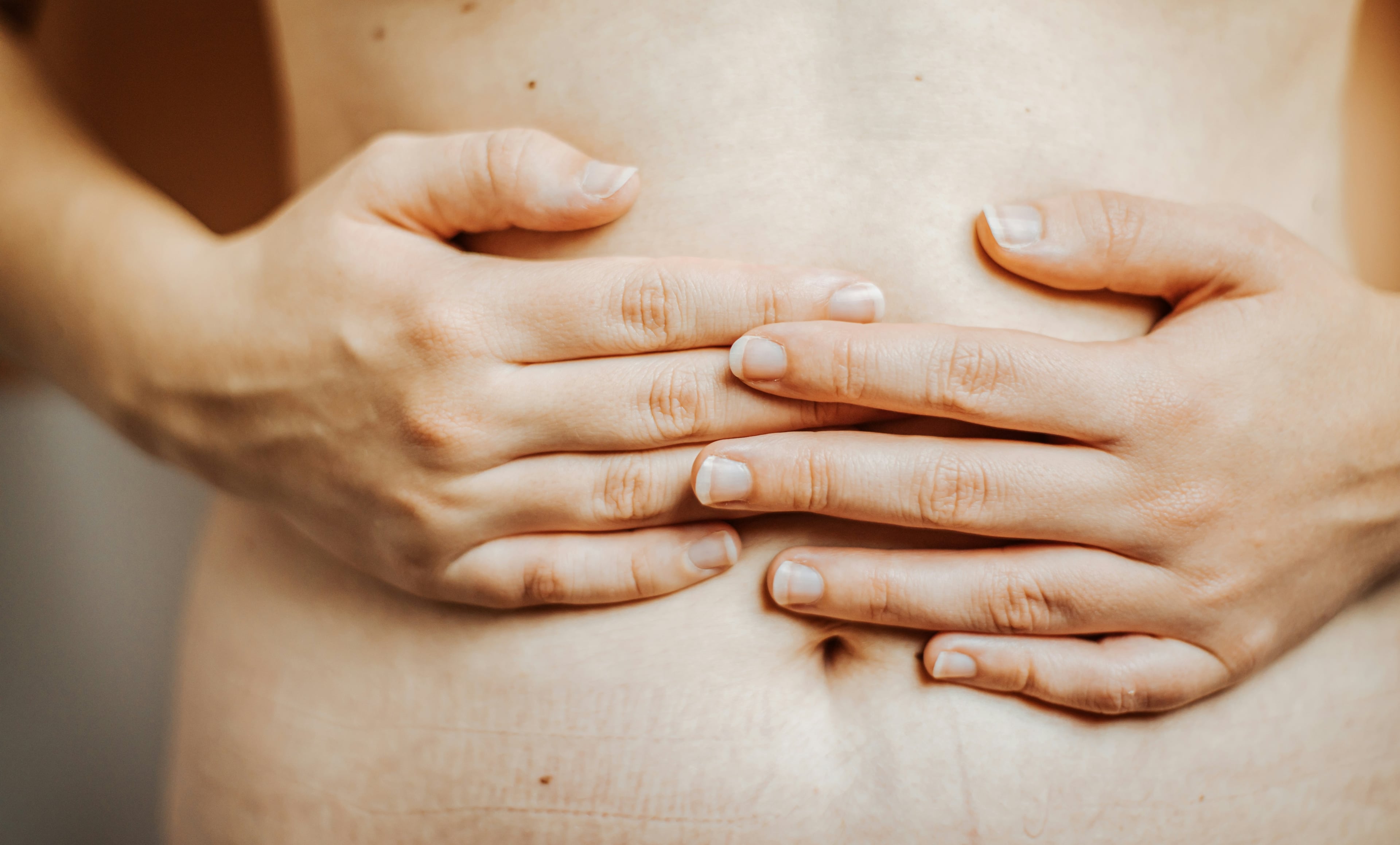Nahaufnahme einer Person, die beide Hände auf den Bauch legt.